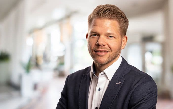 Ein Porträt vom Geschäftsführer Nils Bülte in einem dunklem Anzug und einem weißen Hemd vor einem Büro-Hintergrund.
