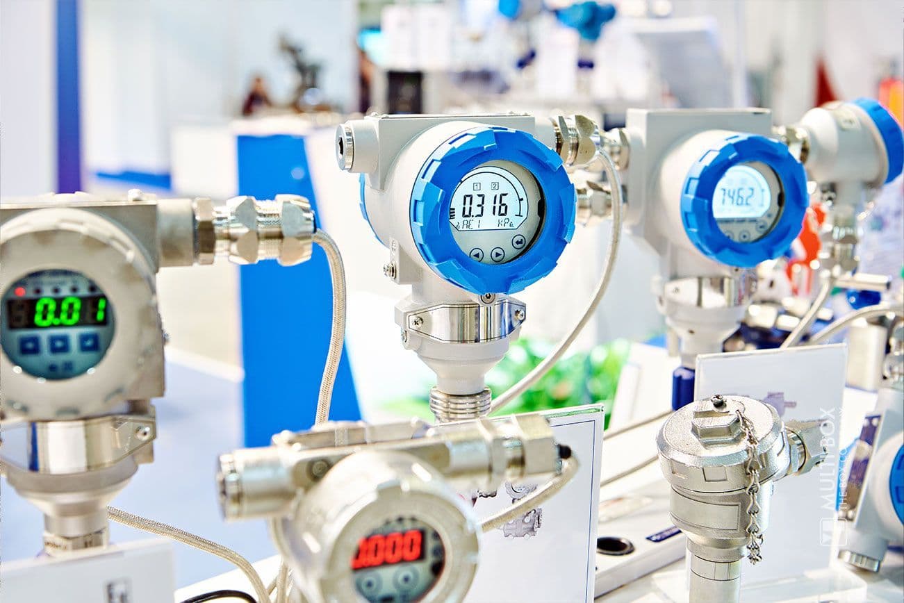 Mehrere industrielle Druckmessgeräte mit Digitalanzeige auf einem Tisch montiert. Die Messgeräte haben blaue und graue Gehäuse und zeigen verschiedene numerische Werte an.