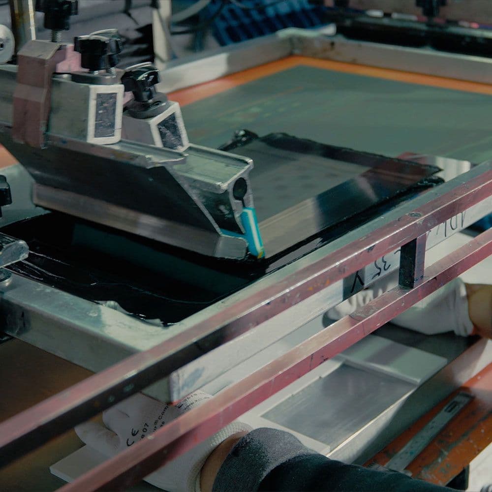 Industrieller Siebdruckprozess mit automatischer Rakel, die schwarze Farbe auf ein Aluminium-Gehäuse aufträgt.